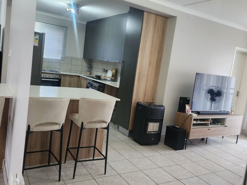 An open-plan living and kitchen area featuring modern cabinetry, a breakfast island, tiled flooring, and a functional kitchen layout.