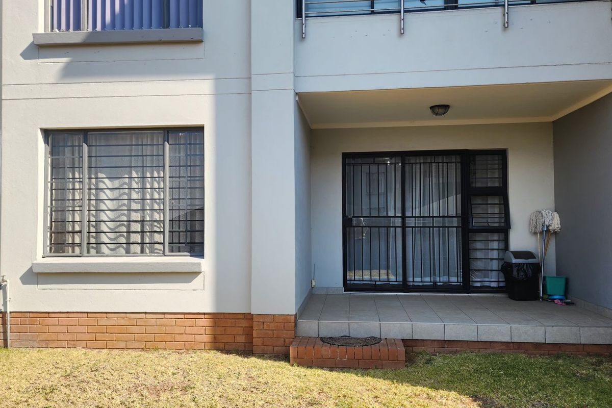 Rear view of the apartment featuring a covered tiled patio, sliding glass doors with security bars, and a brick-accented exterior facade.