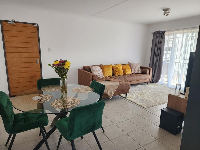 Open plan living and dining area featuring neutral tiled flooring, a wooden entrance door, and a sliding glass door leading to a balcony.
