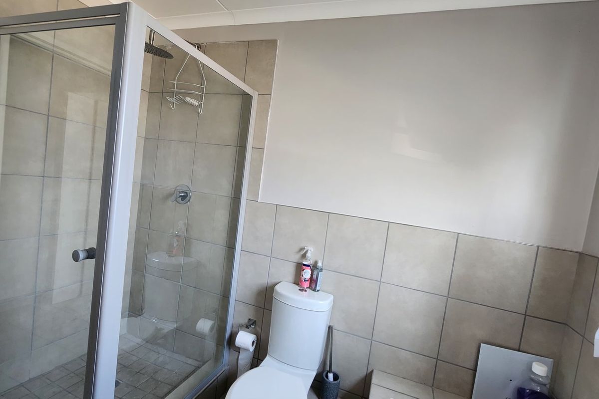 A functional bathroom featuring a glass-enclosed shower, neutral ceramic wall tiling, and a standard toilet suite.