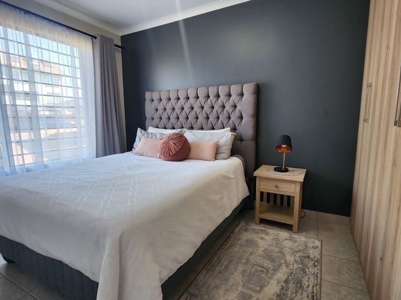 A well-maintained bedroom featuring built-in cupboards, tiled flooring, and a large window with security bars, providing a clean and functional living space.