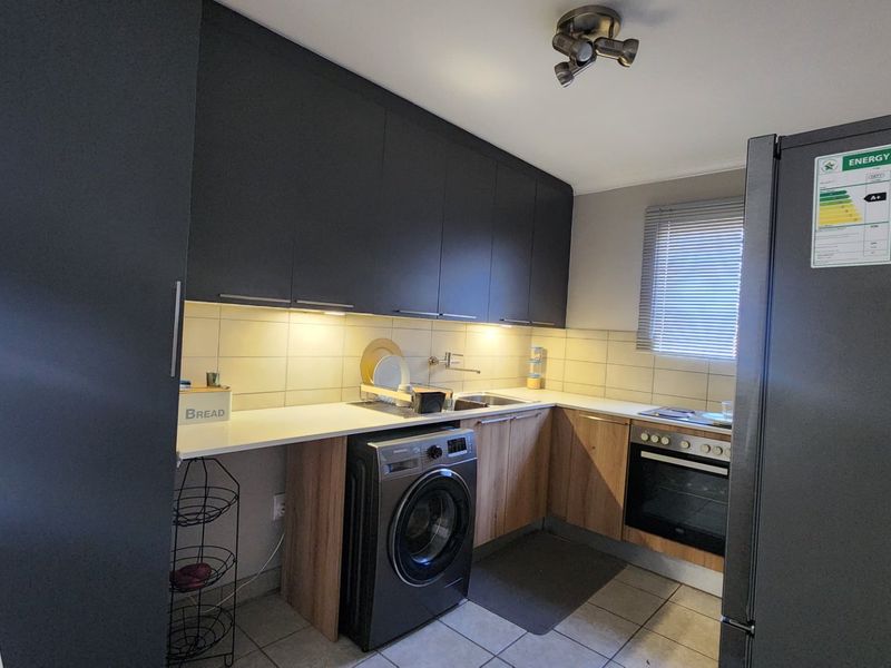 Modern kitchen featuring dark upper cabinetry, wood-finish lower cabinets, integrated oven and hob, tiled backsplash, and under-cabinet lighting.