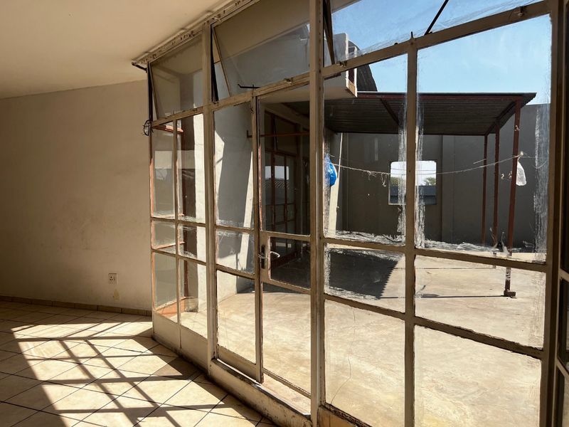 An empty, covered patio area featuring steel-framed glass doors and tiled flooring, requiring maintenance and refurbishment to restore its appeal.