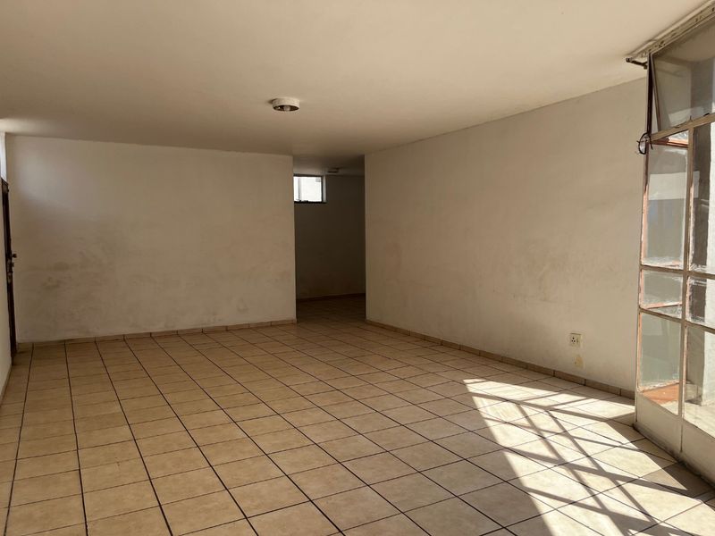 An empty, open-plan living area featuring ceramic tile flooring, neutral walls, and a large metal-framed glass door providing natural light.