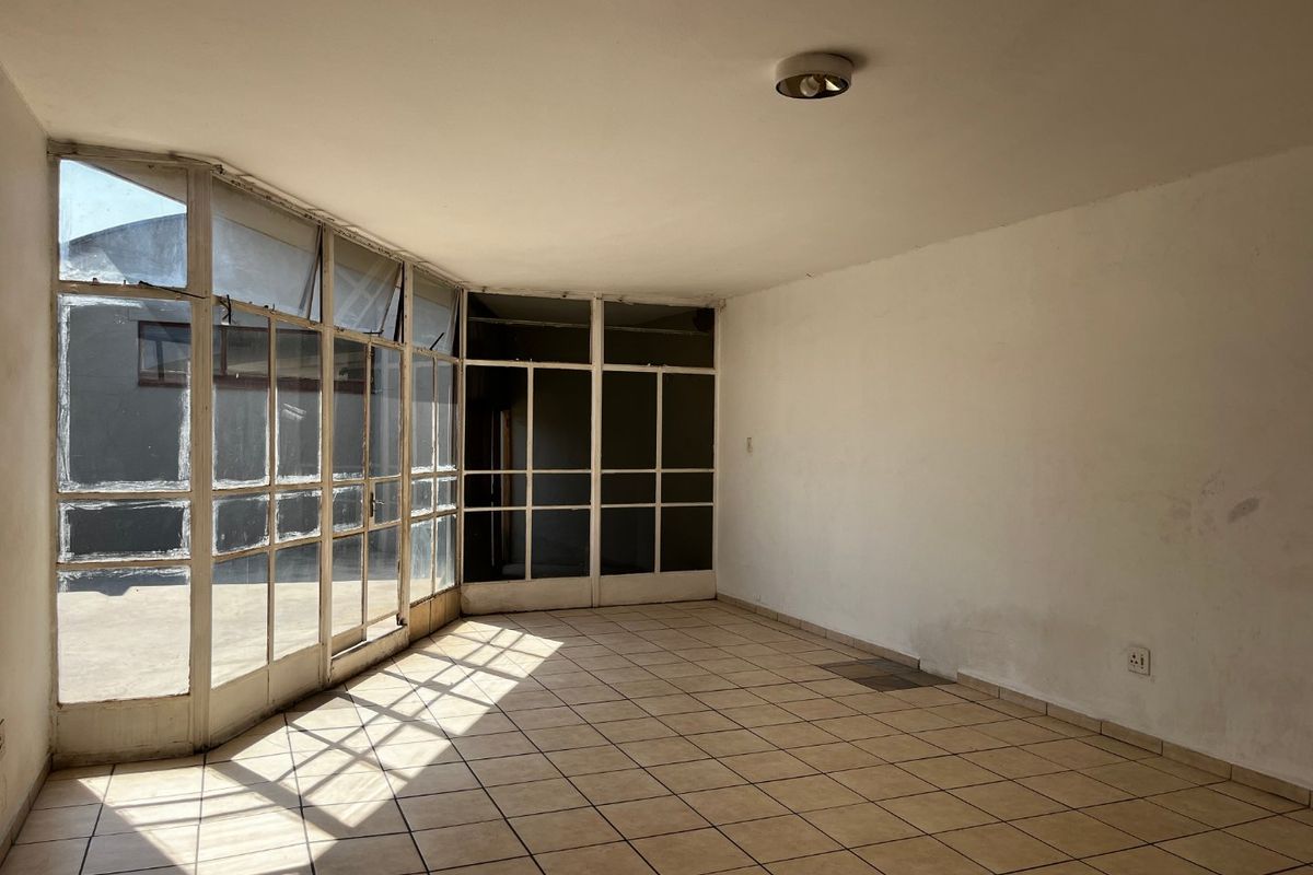 An empty, sunlit living area featuring tiled flooring and extensive glass panel windows and doors, offering a bright, blank canvas for renovation.