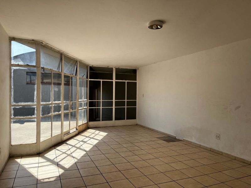 An empty, sunlit living area featuring tiled flooring and extensive glass panel windows and doors, offering a bright, blank canvas for renovation.