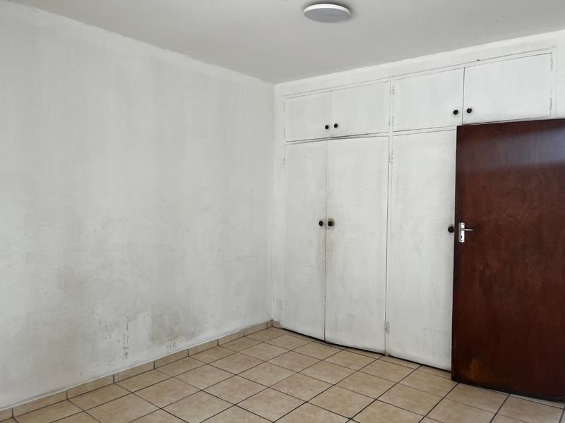 An empty bedroom featuring tiled flooring and built-in storage cupboards, requiring cosmetic updates to the walls and cabinetry.