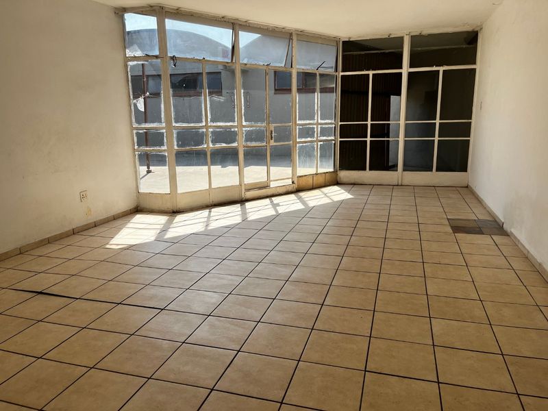 An empty living area featuring ceramic floor tiles and large glass window panels, requiring cosmetic updates and repairs to the flooring and window frames.
