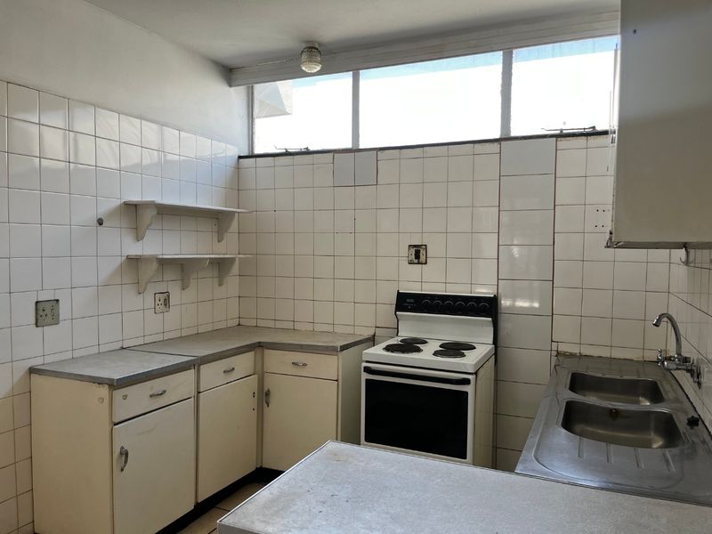A functional, dated kitchen featuring original cabinetry, a stainless steel double sink, and a freestanding electric stove with full-height tiled splashbacks.