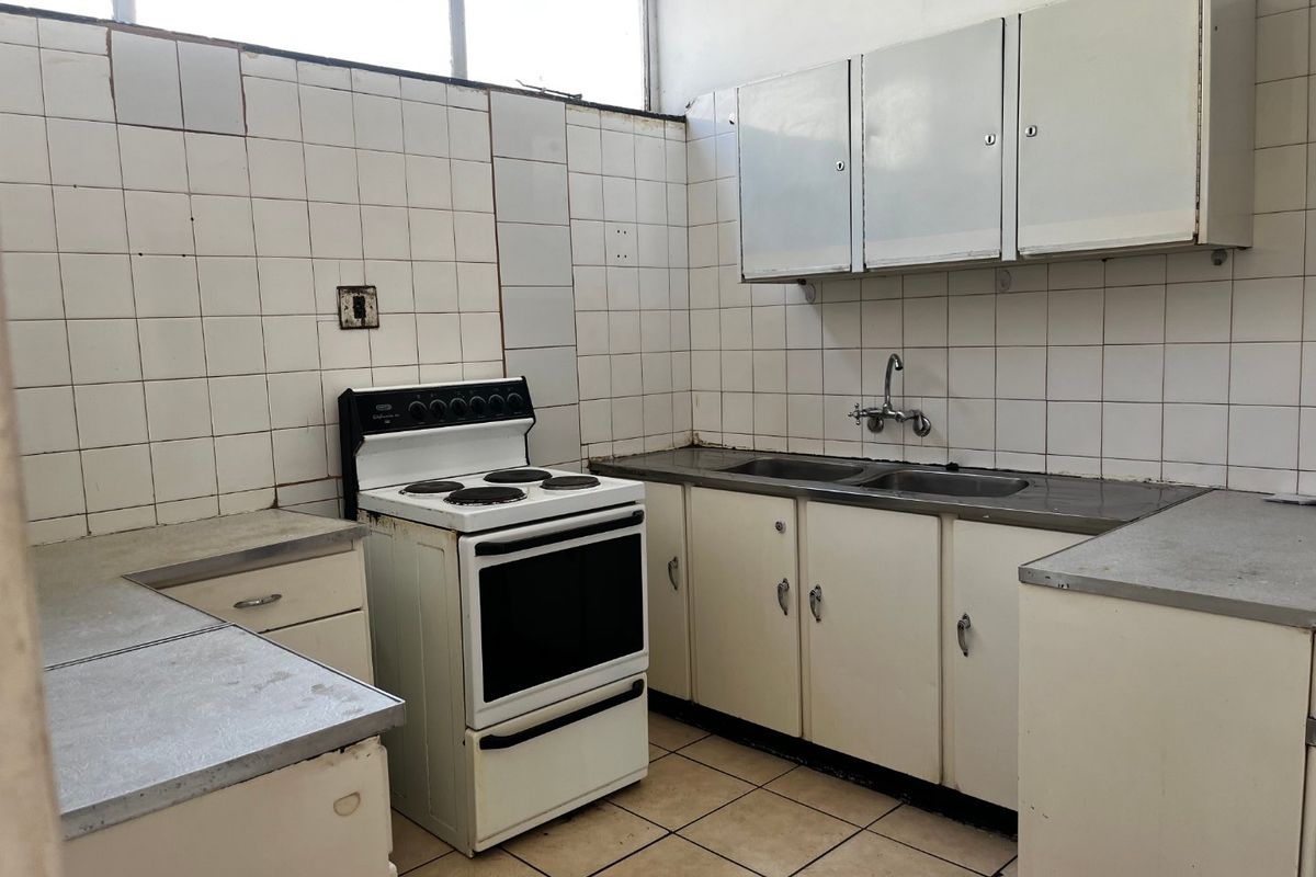 A dated kitchen featuring original cabinetry, a stainless steel double sink, and a freestanding electric stove, requiring significant modernization and cosmetic updates.