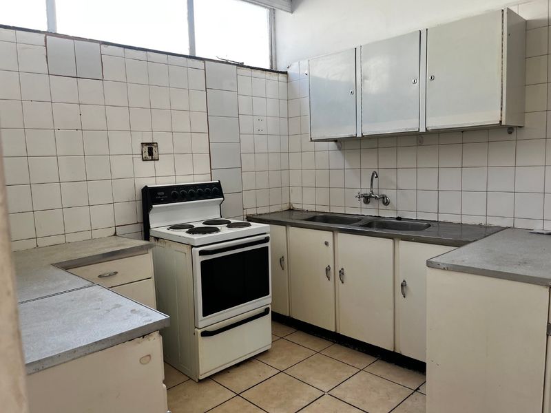 A dated kitchen featuring original cabinetry, a stainless steel double sink, and a freestanding electric stove, requiring significant modernization and cosmetic updates.