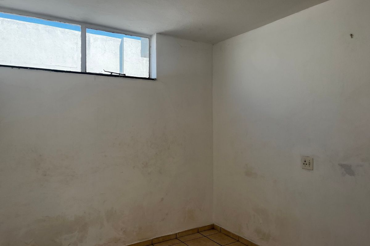 An empty bedroom featuring ceramic tile flooring, a high-level window, and a ceiling light fixture, requiring cosmetic updates to the walls.
