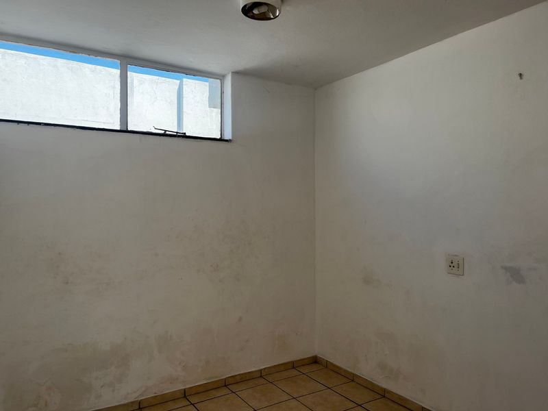 An empty bedroom featuring ceramic tile flooring, a high-level window, and a ceiling light fixture, requiring cosmetic updates to the walls.