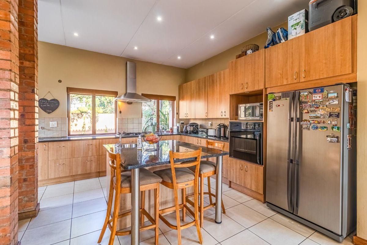 Spacious kitchen featuring light wood cabinetry, granite countertops, a central island, and an exposed brick feature pillar, offering a functional and warm cooking space.