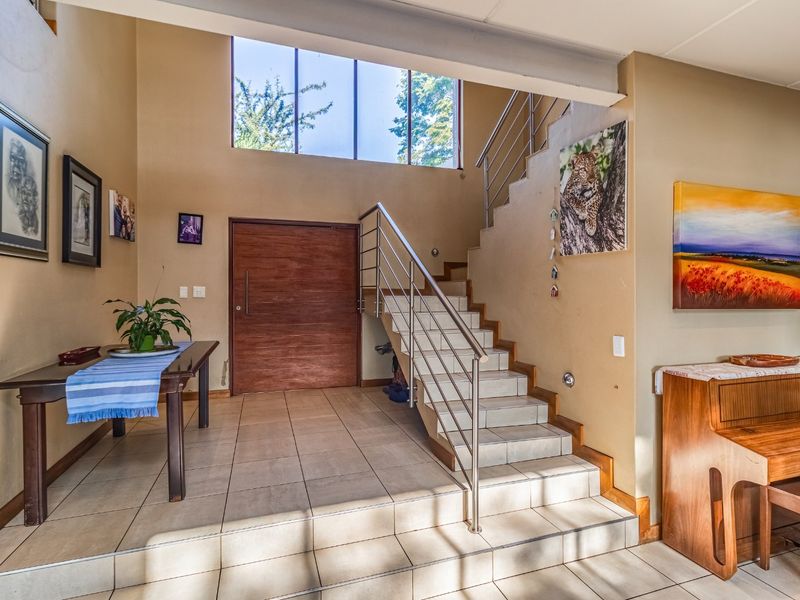 Spacious entrance hall featuring tiled flooring, a modern staircase with stainless steel balustrades, and a large wooden front door with high-level windows.