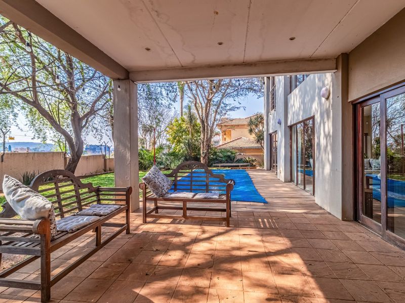 A covered patio area featuring tiled flooring and recessed lighting, providing direct access to the garden and swimming pool through large sliding glass doors.