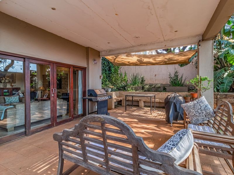 A covered outdoor patio featuring tiled flooring, built-in concrete seating, and direct access to the living area through large sliding glass doors.