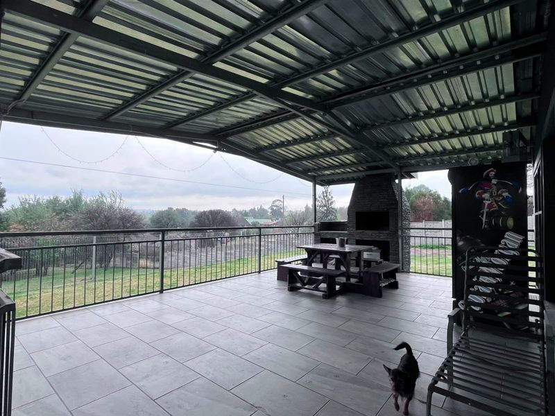 A spacious covered patio featuring tiled flooring, a built-in stone fireplace, and metal railings, offering an expansive view of the surrounding farm landscape.