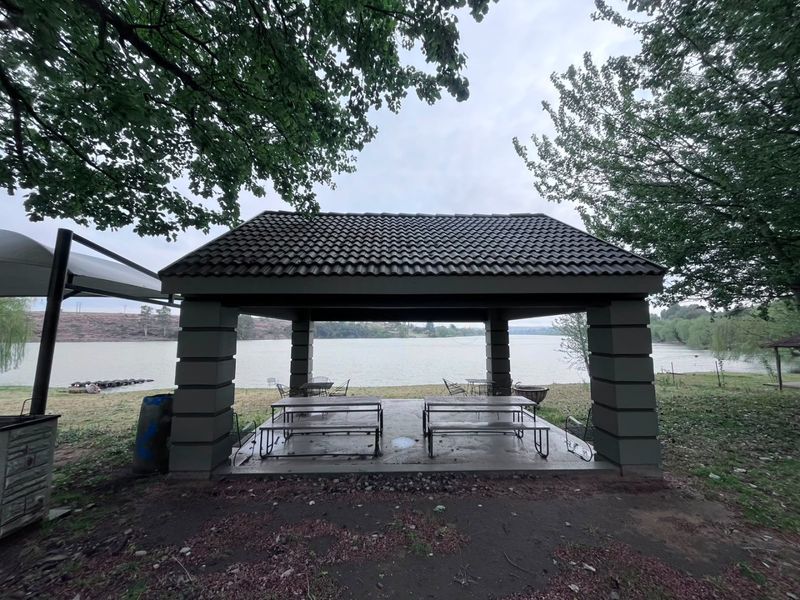 A covered outdoor entertainment pavilion featuring a tiled roof and concrete pillars, situated directly overlooking the waterfront.