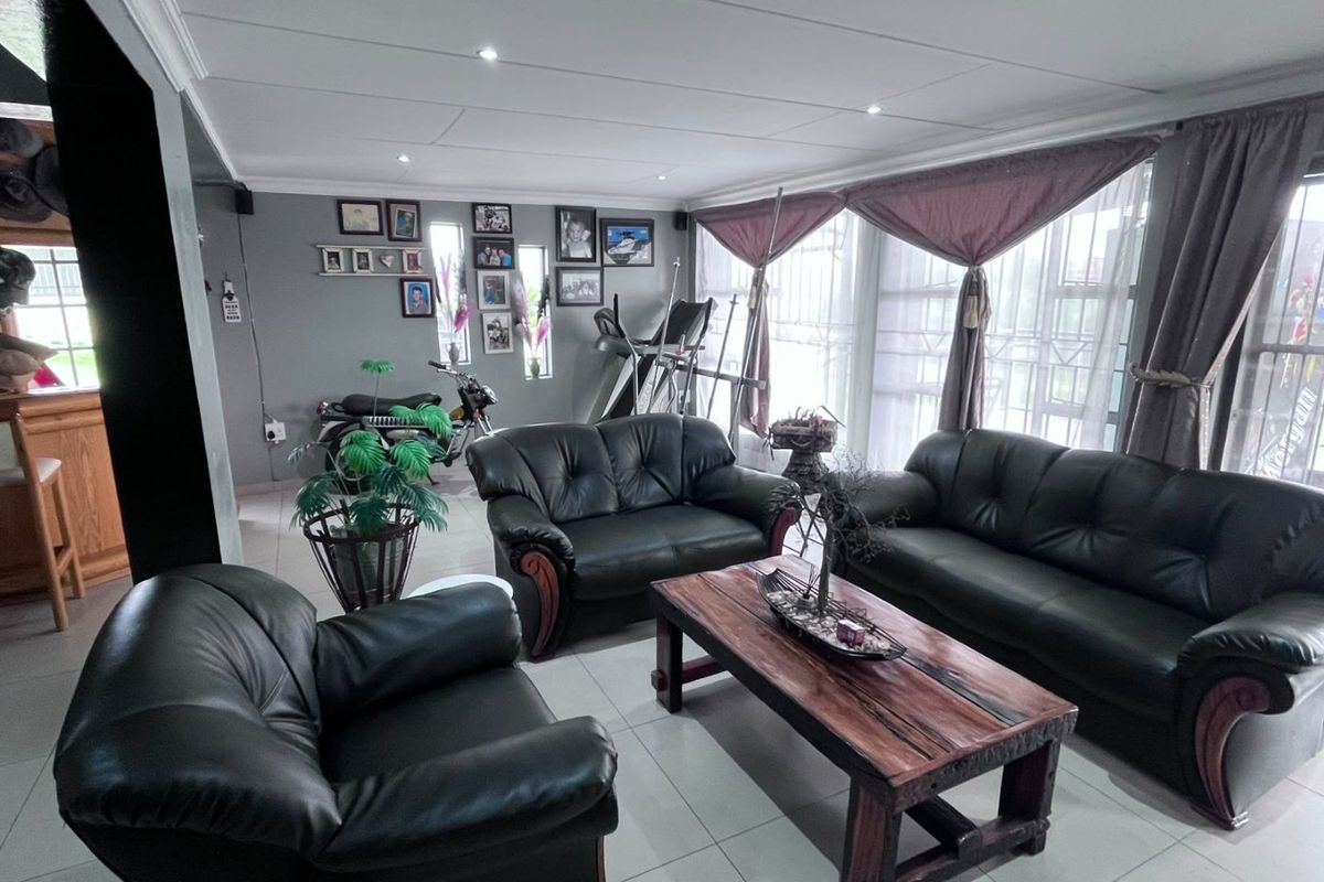 A spacious living room featuring tiled flooring, recessed ceiling lighting, and large windows with security bars, offering a functional and well-lit living space.