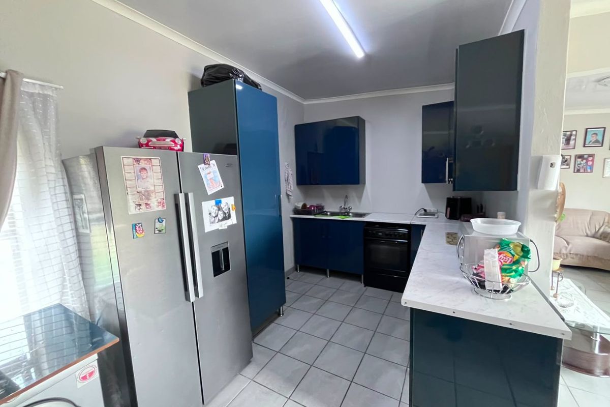 A functional kitchen featuring dark blue cabinetry, laminate countertops, tiled flooring, and a stainless steel sink with an integrated oven.