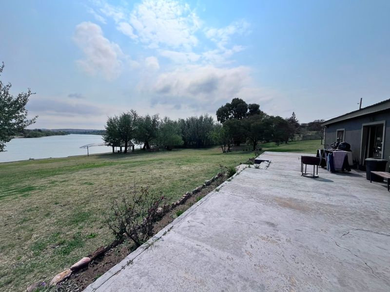 Spacious concrete rear patio overlooking a scenic riverfront landscape, offering expansive outdoor space and direct access to the natural surroundings.