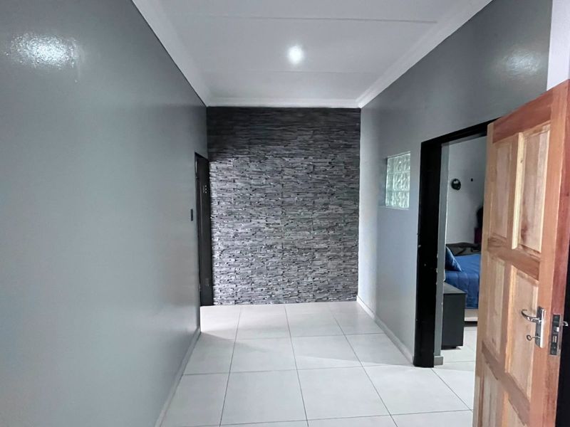 A clean, modern hallway featuring a textured stone accent wall, neutral grey painted walls, and light ceramic floor tiles.