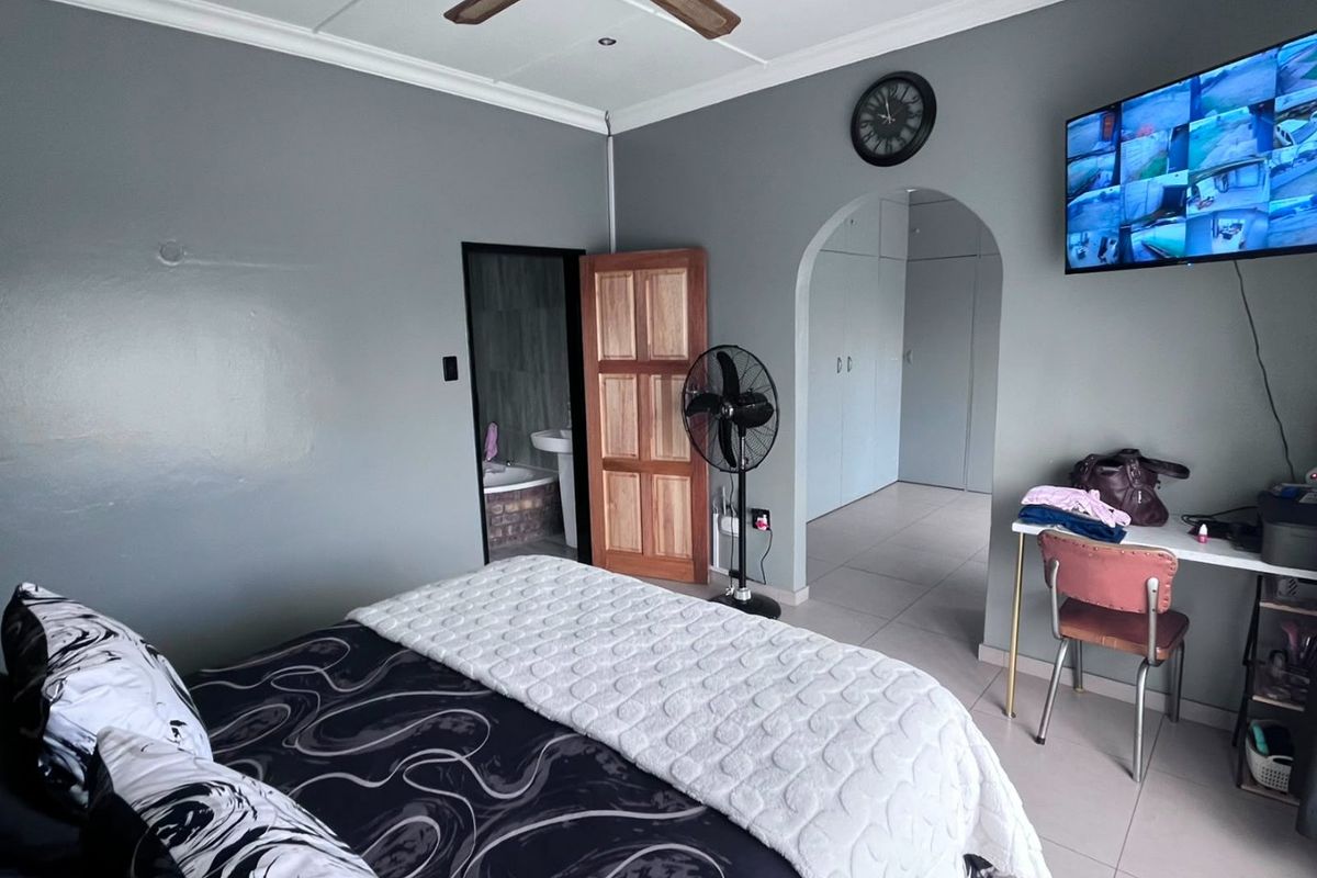 Spacious bedroom featuring tiled flooring, a ceiling fan, and an arched entryway leading to a dressing area with built-in cupboards.