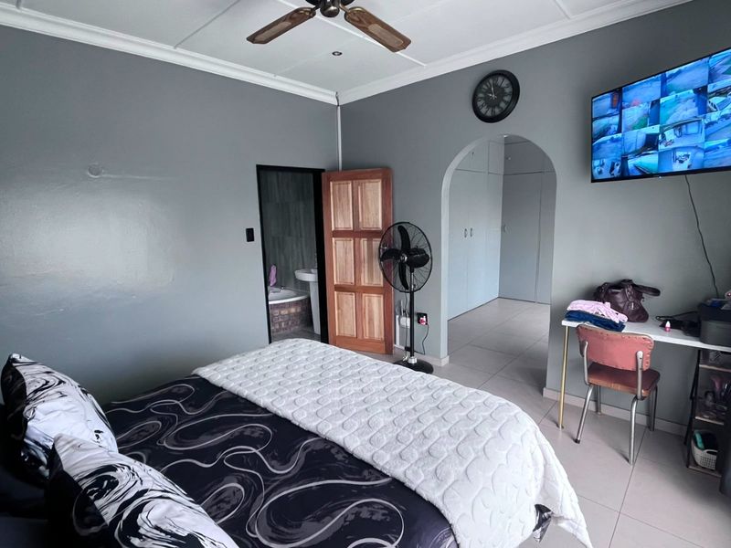 Spacious bedroom featuring tiled flooring, a ceiling fan, and an arched entryway leading to a dressing area with built-in cupboards.