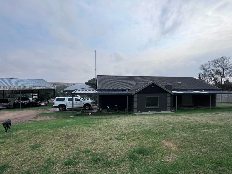 Front view of a farm-style residence featuring a dark-toned exterior, corrugated metal roofing, and an attached covered carport area.
