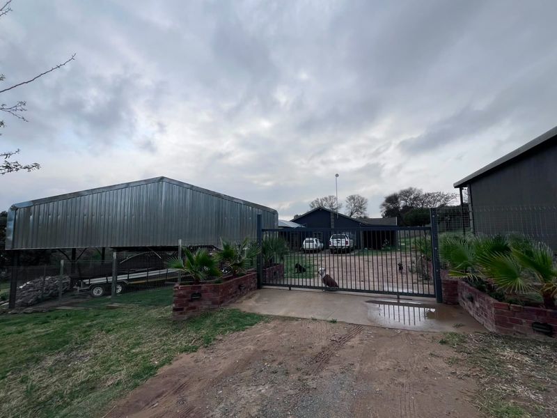 Front entrance of the farm property featuring a secure metal gate, brick pillars, and a large metal storage shed on the driveway.