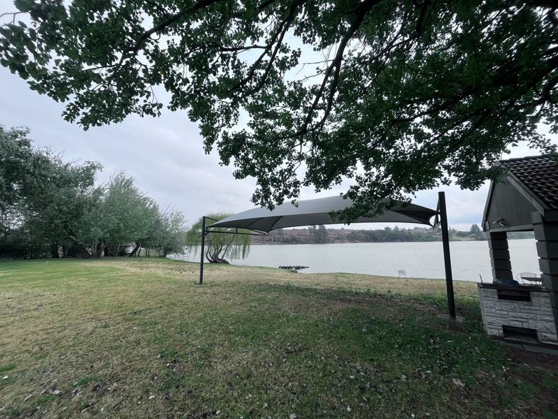 Rear garden area featuring a shade sail, built-in stone-clad braai, and direct access to the waterfront.