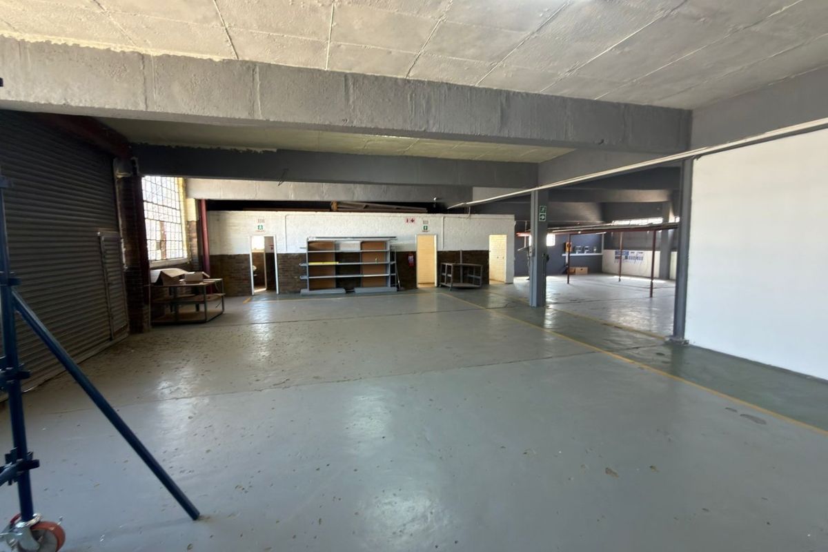 Spacious industrial utility area featuring concrete flooring, exposed structural beams, and a roller shutter door, suitable for storage or workshop use.