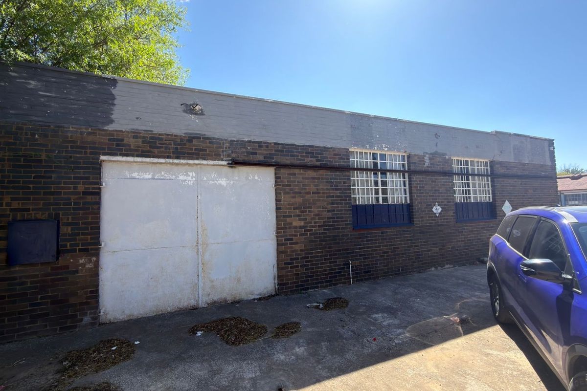 Rear exterior view of a commercial brick building featuring a large sliding metal door, security-barred windows, and a concrete apron.