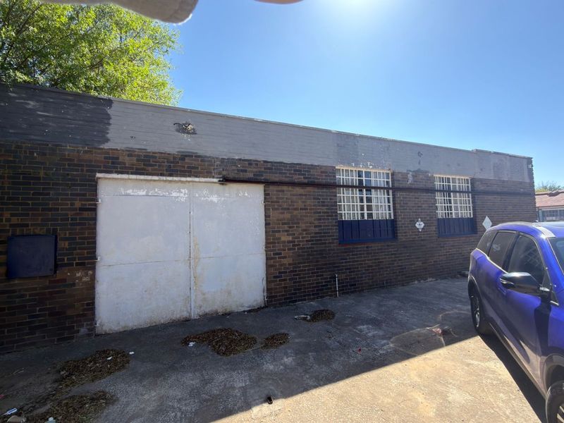 Rear exterior view of a commercial brick building featuring a large sliding metal door, security-barred windows, and a concrete apron.