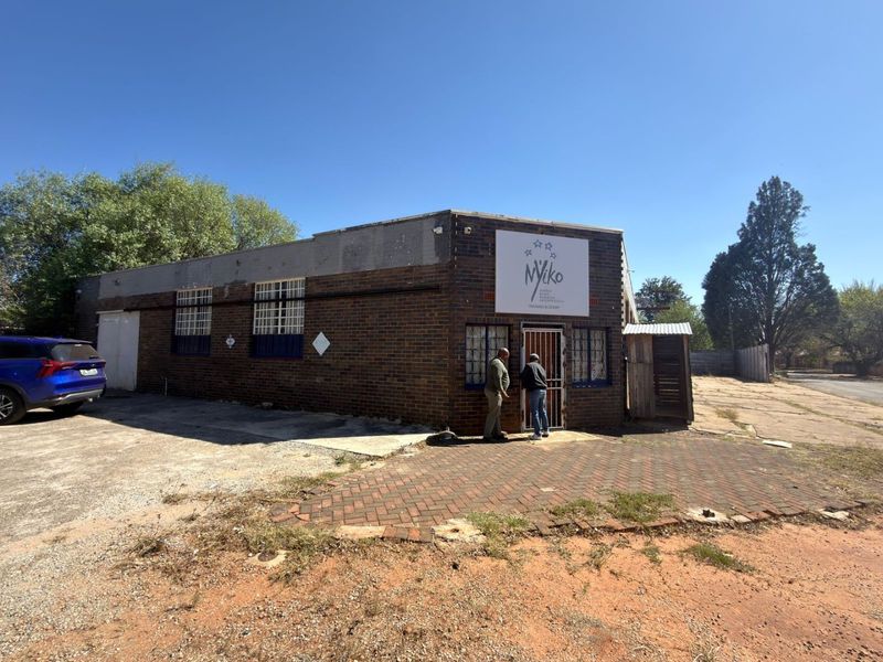 Front exterior view of a commercial brick building featuring a paved driveway, security gate, and prominent signage.