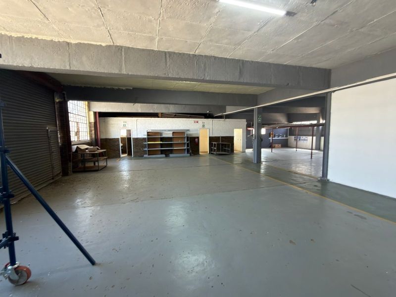 Spacious industrial utility area featuring concrete flooring, exposed structural beams, and a roller shutter door, suitable for storage or workshop use.