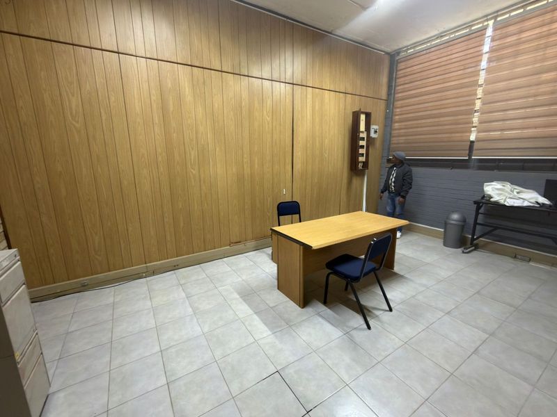 A functional office space featuring wood-paneled walls, tiled flooring, and large windows with roller blinds, suitable for a professional workspace.
