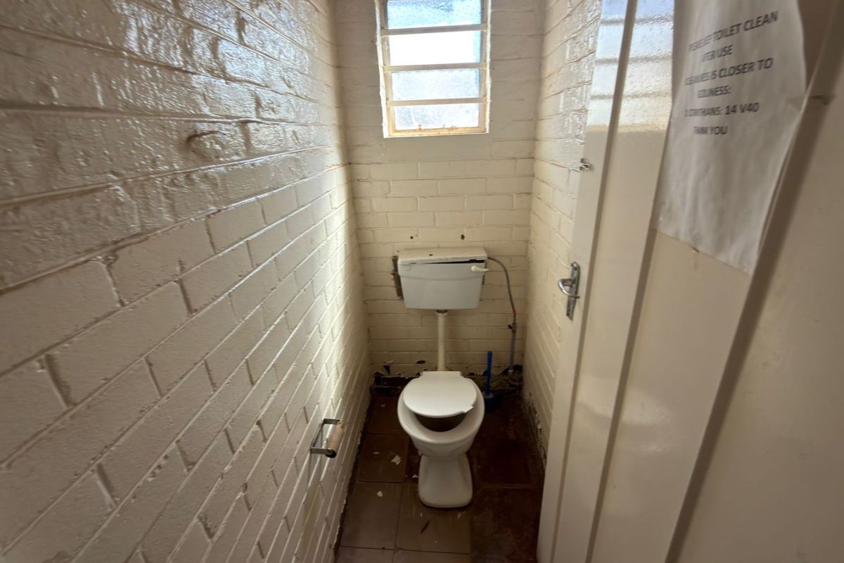 A small, utilitarian restroom featuring painted brick walls, a standard toilet, and a small window with security bars.