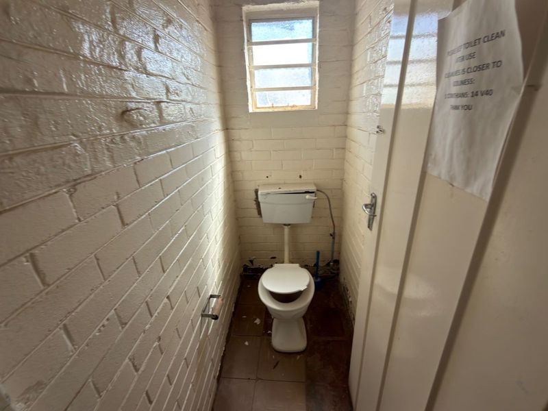 A small, utilitarian restroom featuring painted brick walls, a standard toilet, and a small window with security bars.