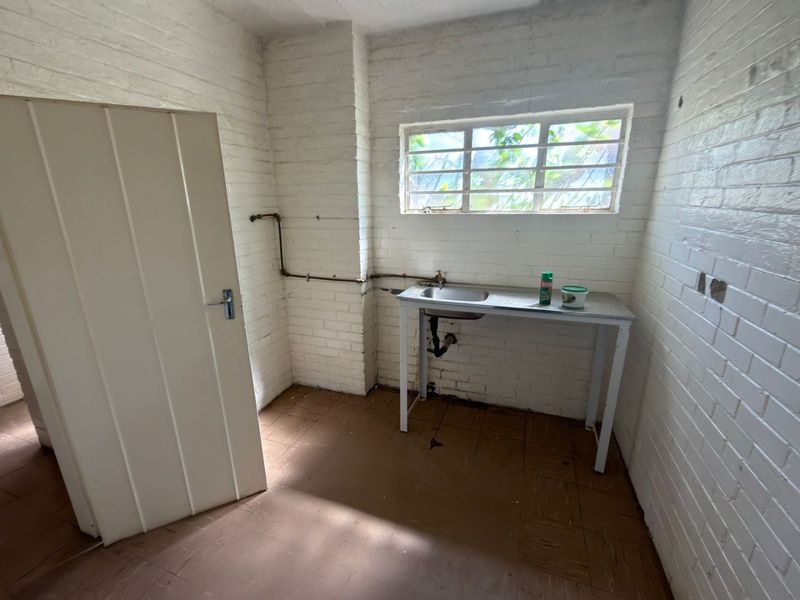 A basic utility or scullery area featuring painted brick walls, tiled flooring, and a simple stainless steel sink unit with exposed plumbing.