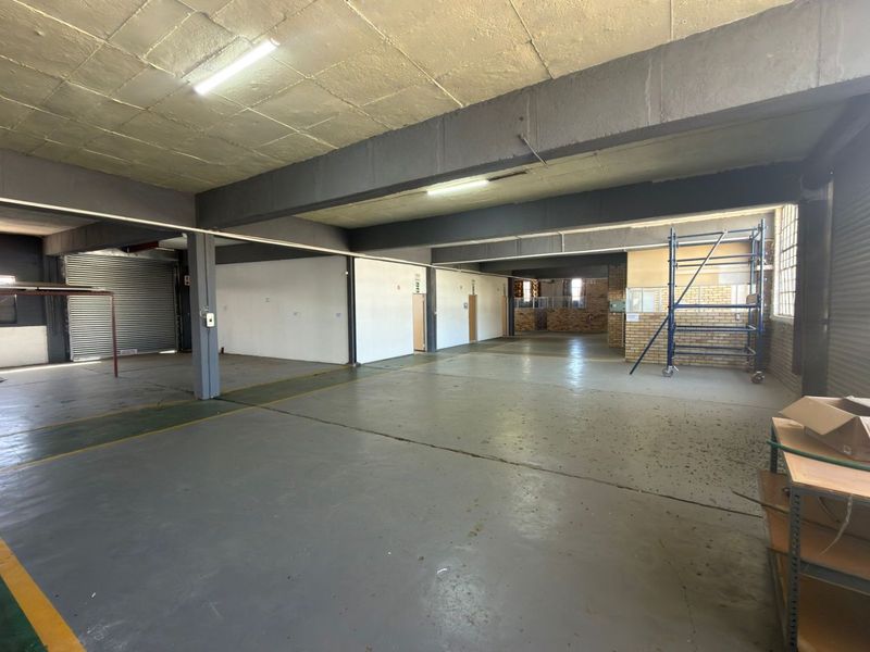Spacious industrial utility area featuring exposed concrete ceilings, steel support beams, durable concrete flooring, and a large roller shutter door for easy access.