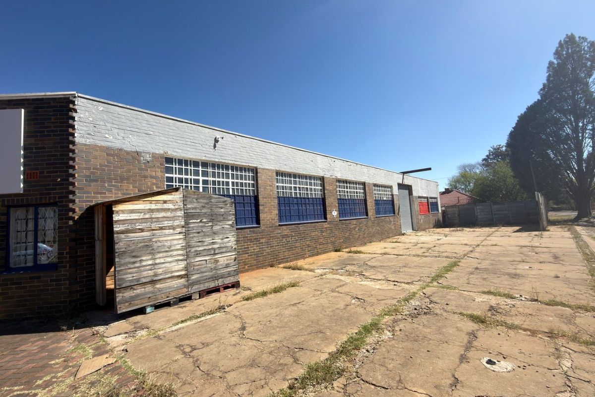 Rear exterior view of a commercial property featuring a brick facade, industrial roller shutter door, and a large concrete yard area.