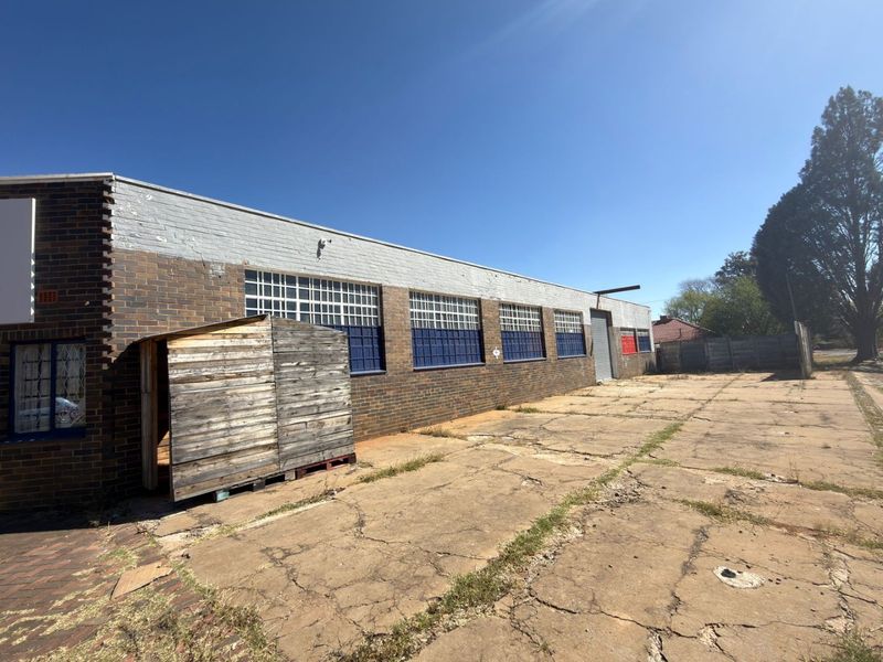 Rear exterior view of a commercial property featuring a brick facade, industrial roller shutter door, and a large concrete yard area.