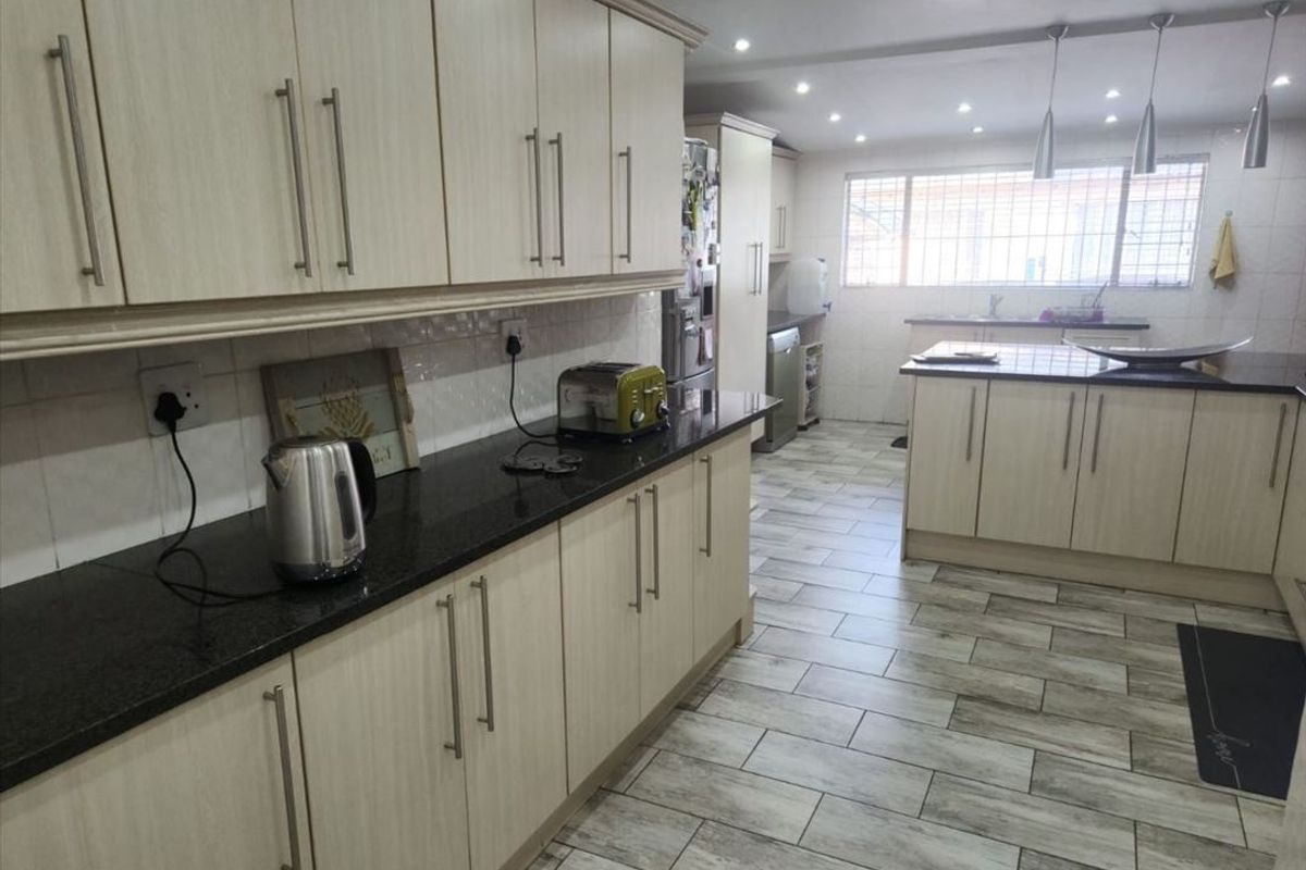 Spacious modern kitchen featuring light wood-finish cabinetry, dark granite countertops, tiled flooring, and ample recessed lighting throughout the workspace.