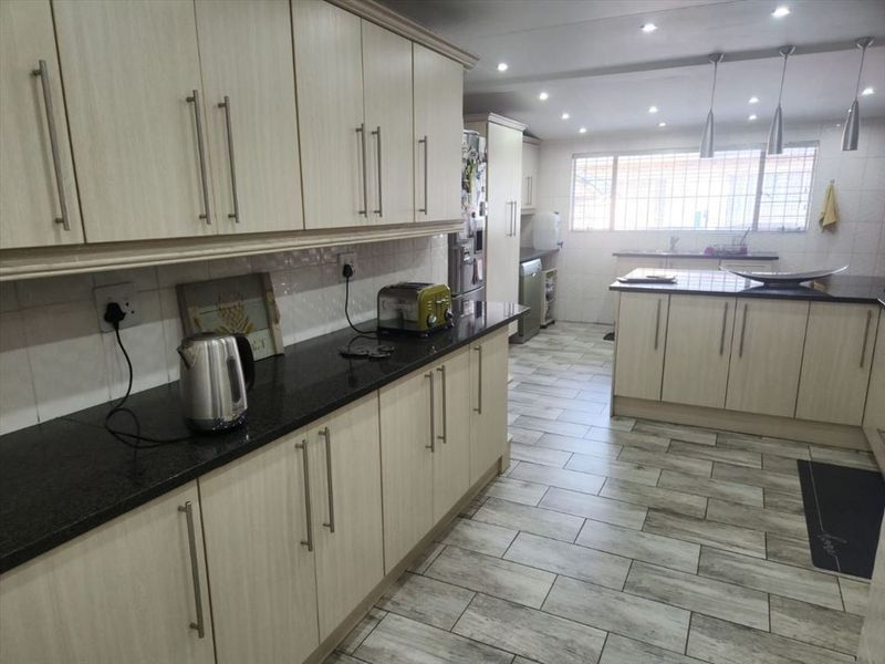 Spacious modern kitchen featuring light wood-finish cabinetry, dark granite countertops, tiled flooring, and ample recessed lighting throughout the workspace.