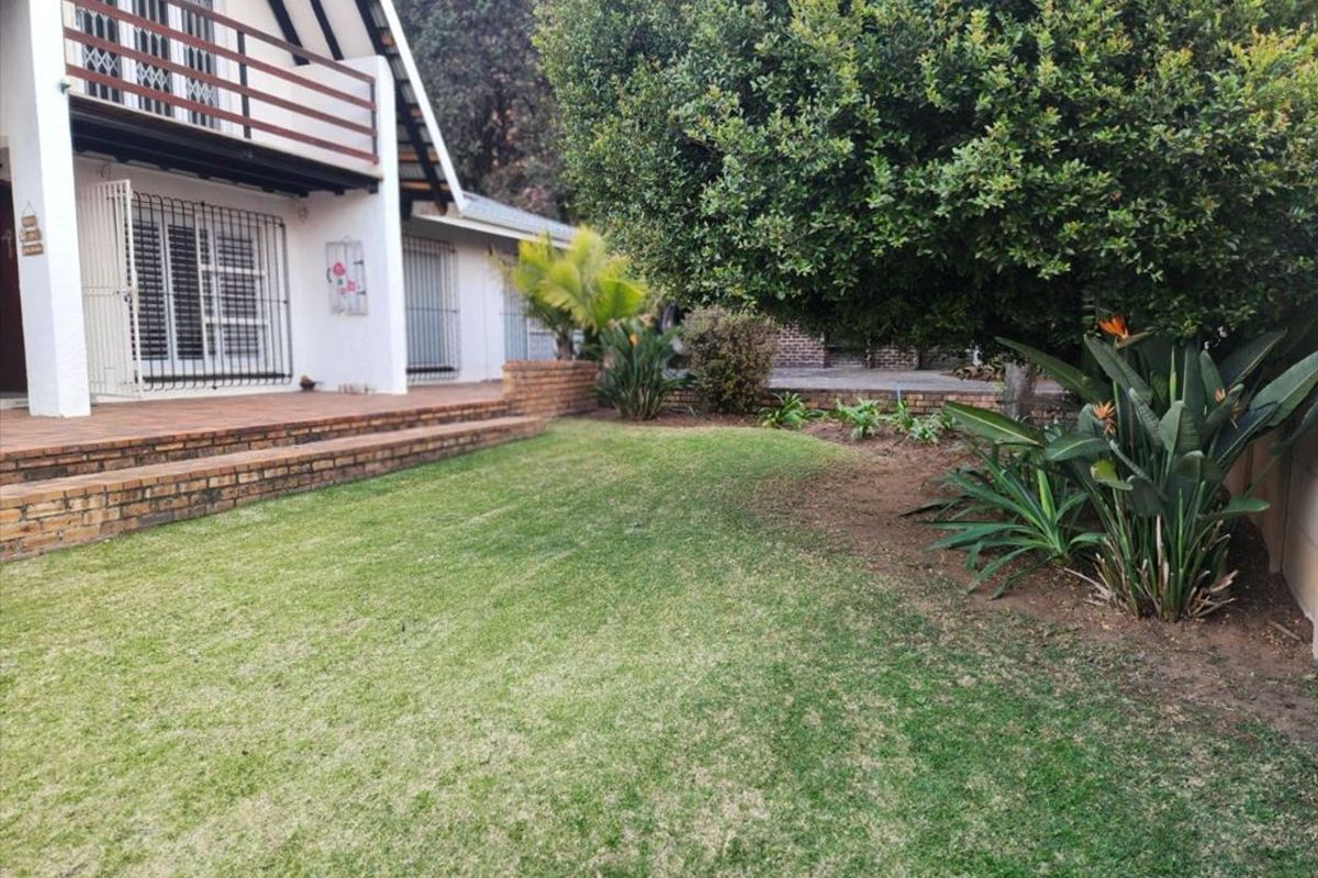 A view of the rear garden featuring a brick patio, a balcony on the upper level, and established landscaping.