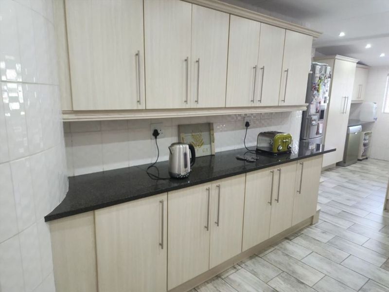 A functional kitchen featuring light-toned laminate cabinetry, dark granite countertops, a tiled backsplash, and modern tiled flooring with recessed ceiling lighting.