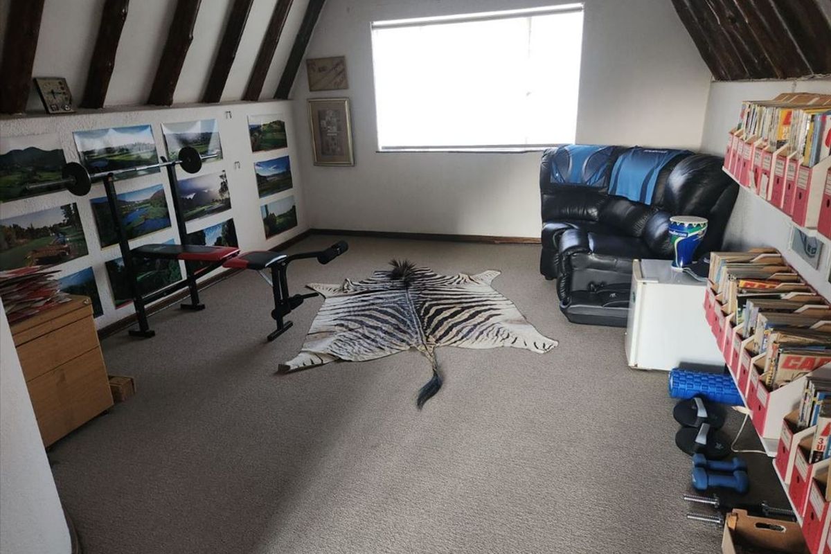 An attic-style bedroom featuring exposed timber rafters, sloped ceilings, and carpeted flooring, currently utilized as a multi-purpose hobby and exercise space.