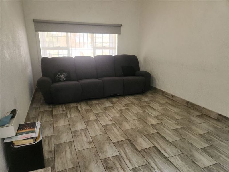 A living room featuring wood-look tiled flooring, a window with security bars, and a roller blind.
